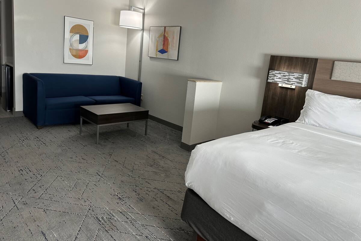Habitación de hotel con una cama, un sofá azul, una mesita y dos lámparas fijadas a la pared.