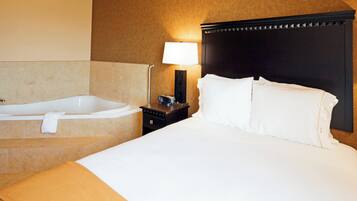 Habitación de hotel con una cama grande, una bañera separada, una mesita de noche con lámpara y un reloj de pared.