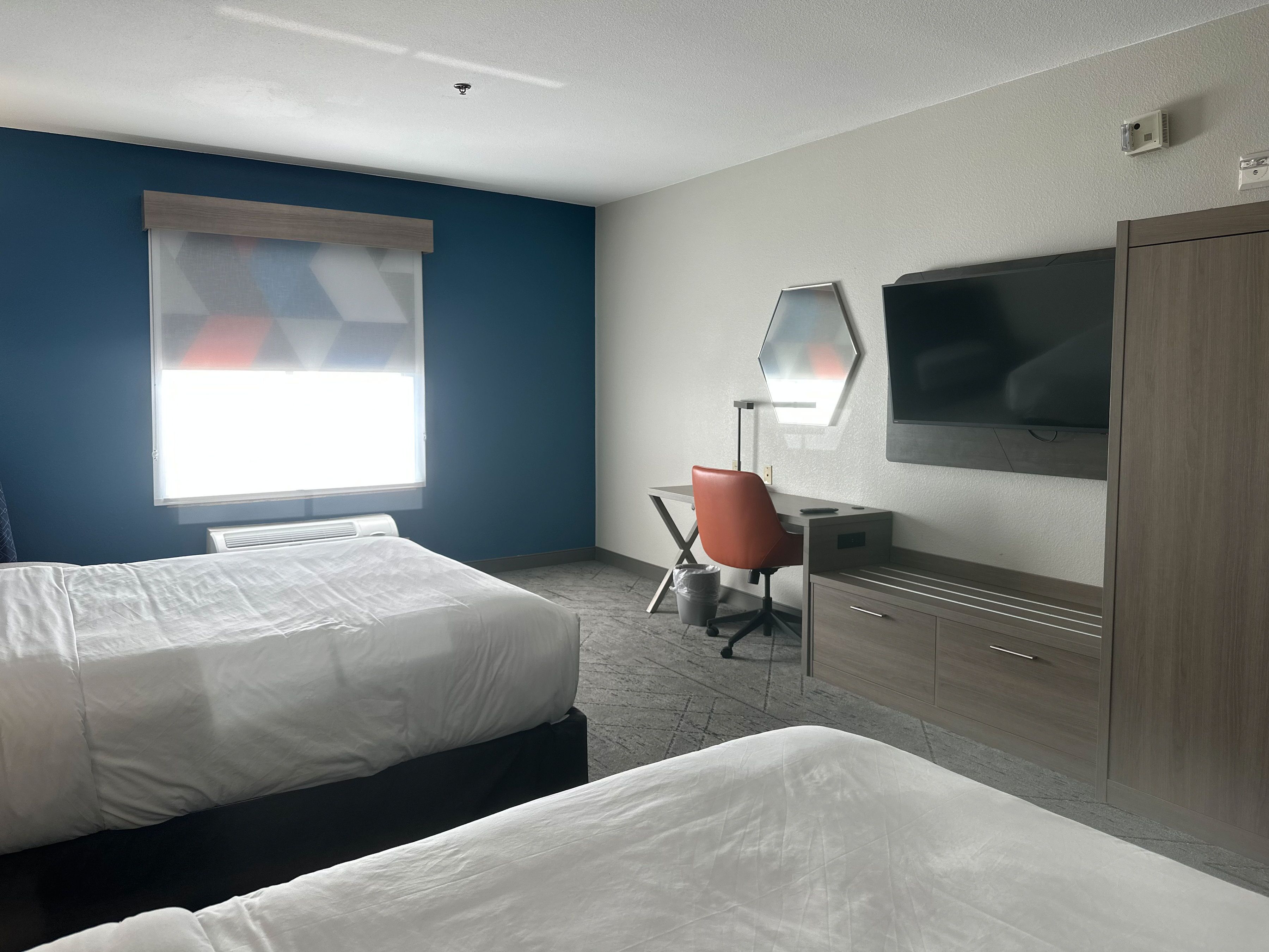 A hotel room with two beds, a desk, a chair, a TV, and a wardrobe.