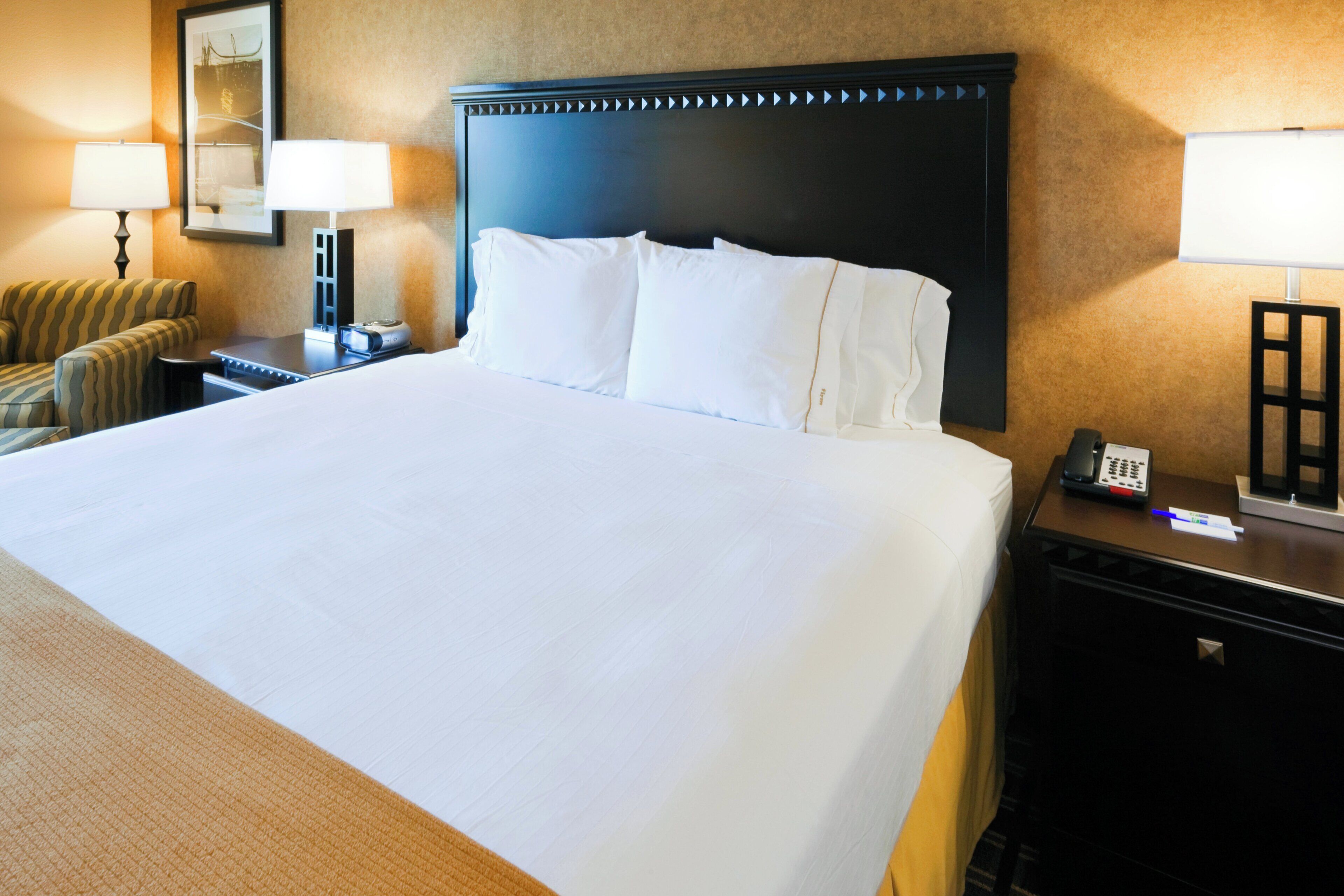 A hotel room with a large bed, a nightstand, a lamp, a chair, and a desk with a telephone.