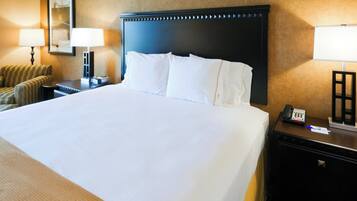 A hotel room with a large bed, a nightstand, a lamp, a chair, and a desk with a telephone.