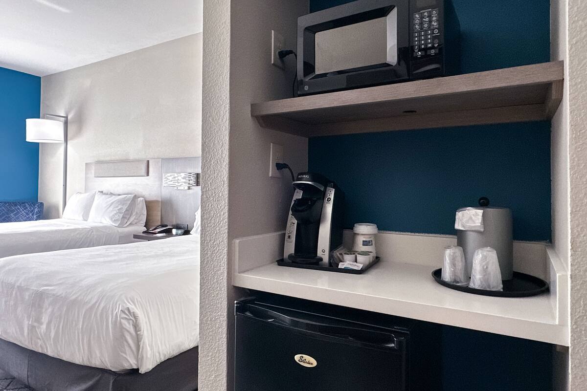 Habitación de hotel con dos camas, minibar, cafetera y microondas.