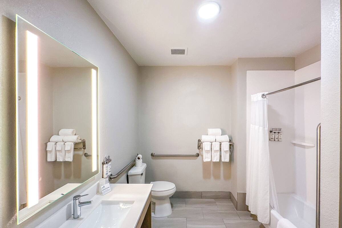 Un baño moderno con un espejo grande, un lavamanos, un inodoro y una zona de ducha.