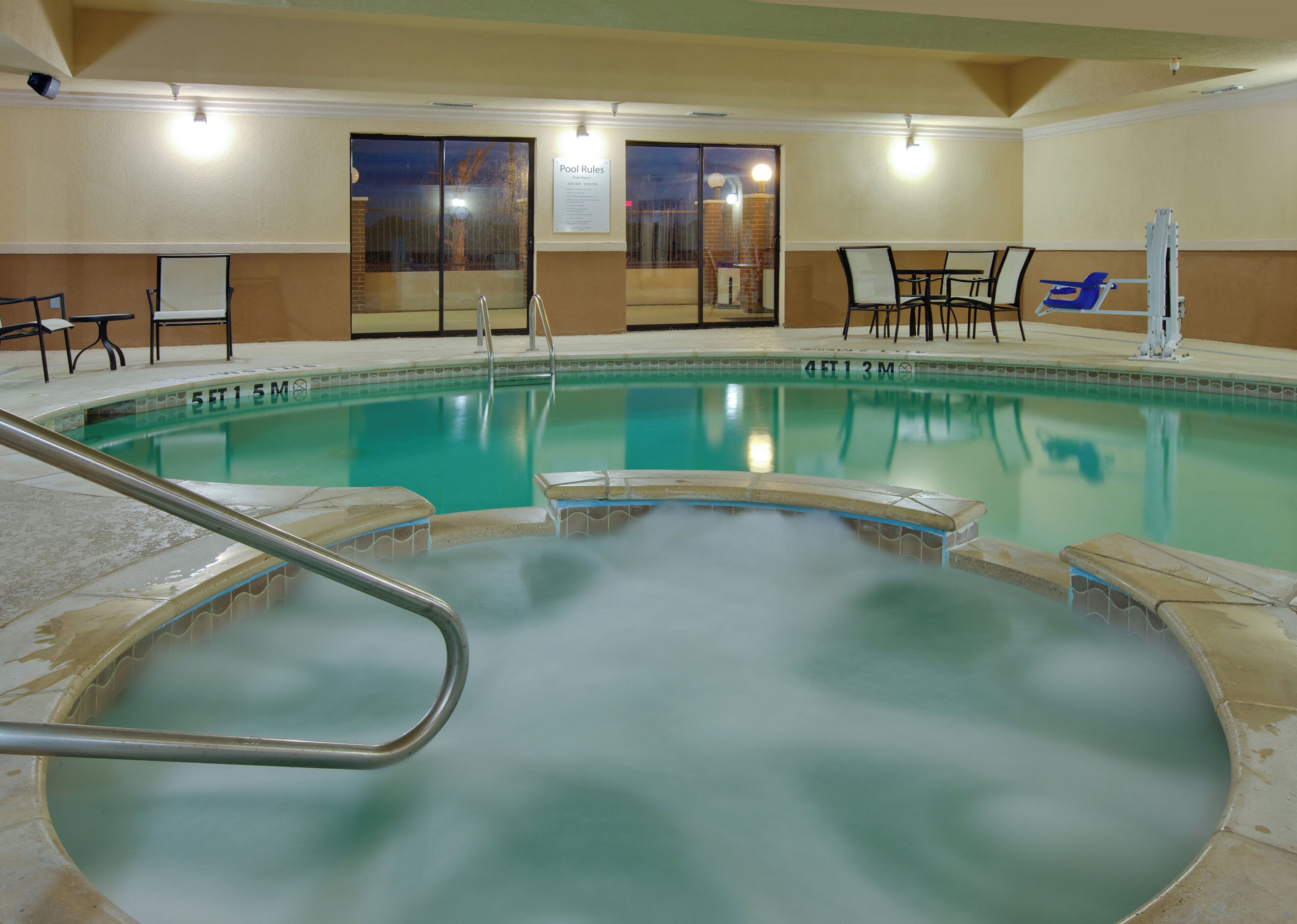 Piscina con zona de hidromasaje, cartel con las normas de la piscina y asientos junto a la piscina.