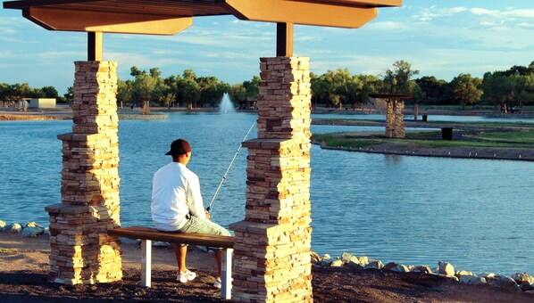 A person sitting on a stone bench with a view of a lake and trees in the background. - Isleta Resort and Casino (Albuquerque)