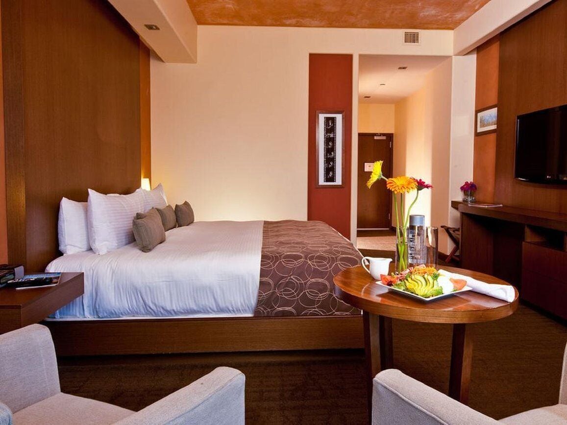 Una camera d'hotel con un letto, un tavolino rotondo con un vassoio di cibo, una TV e una testiera di legno.
