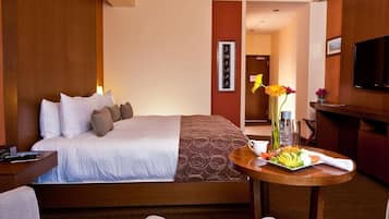 Una camera d'hotel con un letto, un tavolino rotondo con un vassoio di cibo, una TV e una testiera di legno.