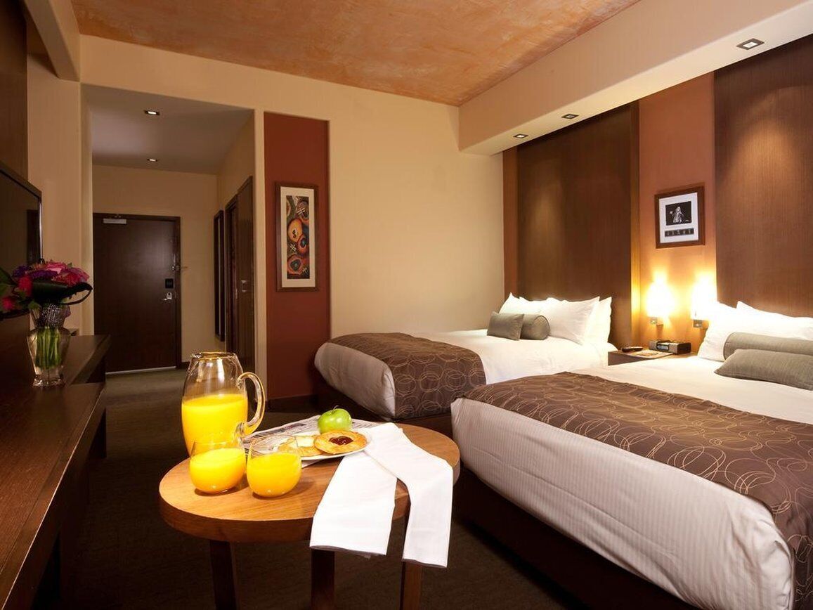Een hotelkamer met twee bedden, een houten tafel met ontbijtartikelen en een nachtkastje met een lamp.