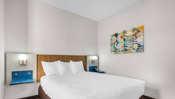 Una habitación de hotel con una cama grande, dos mesitas de noche, un cabecero, una obra de arte colgada en la pared y un velador con lámpara.