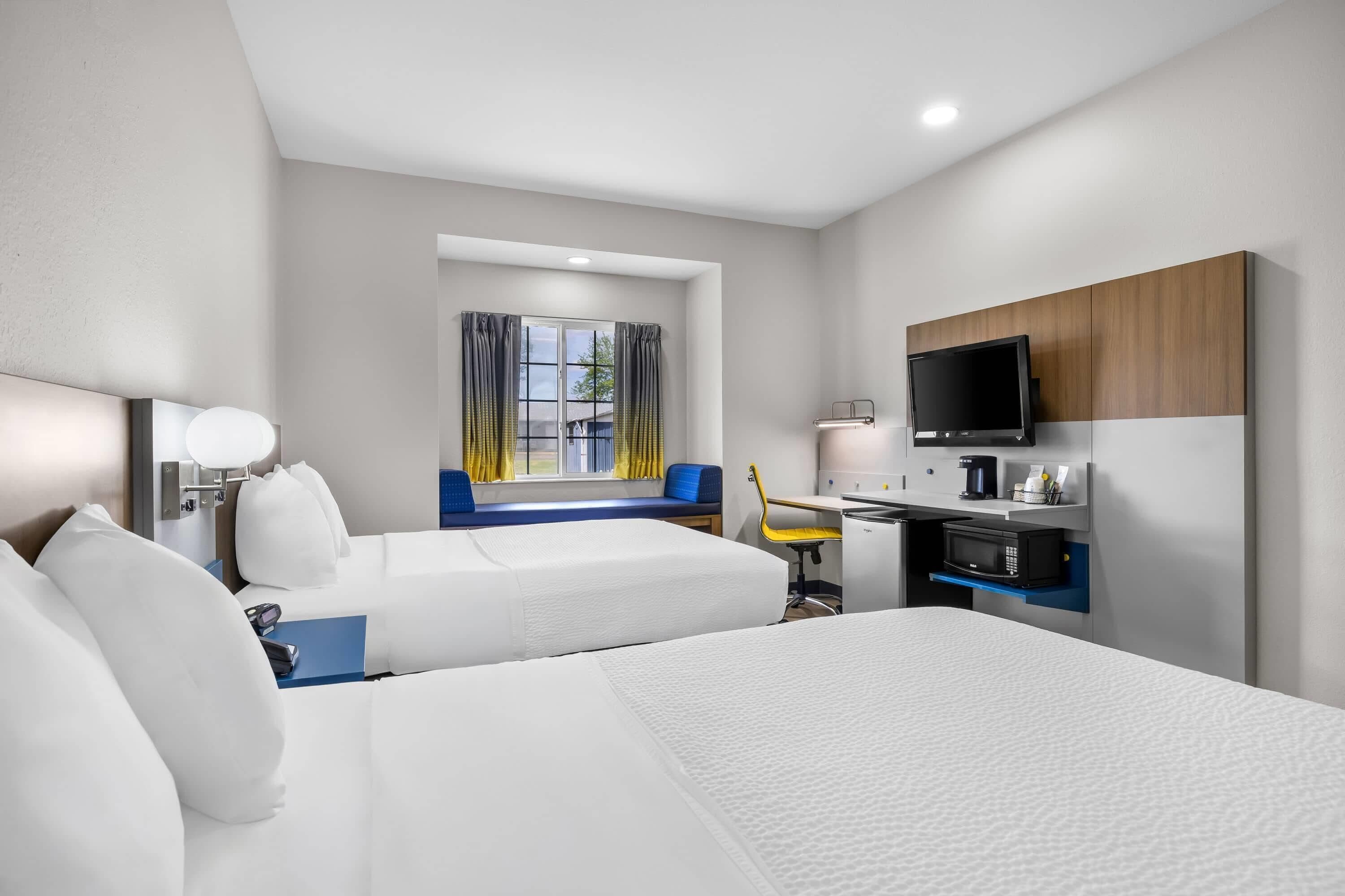 A hotel room with two beds, a desk with a chair, a television, and a window with curtains.