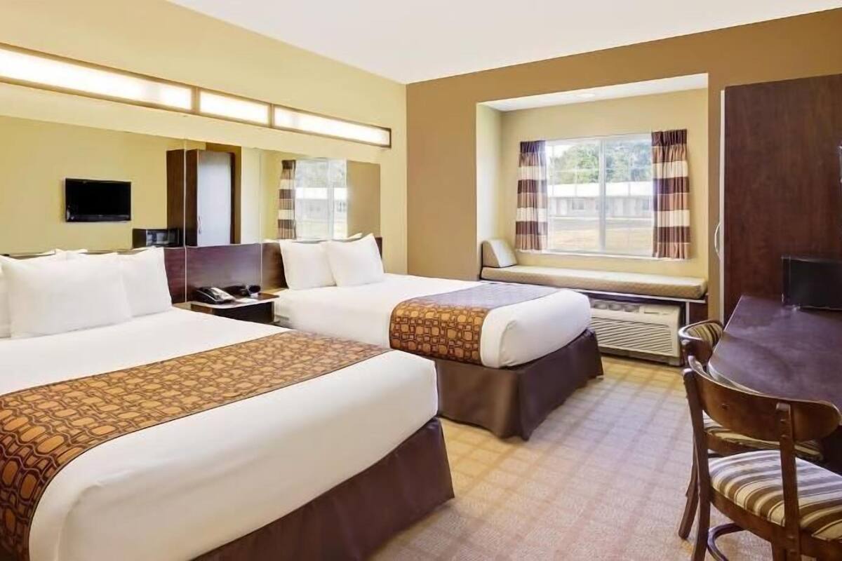 A hotel room with two beds, a desk, a chair, a TV, and a window with curtains.