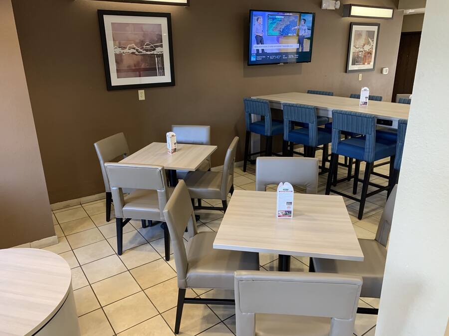 A restaurant with multiple tables and chairs, a television mounted on the wall displaying a news channel, and framed artwork on the walls.