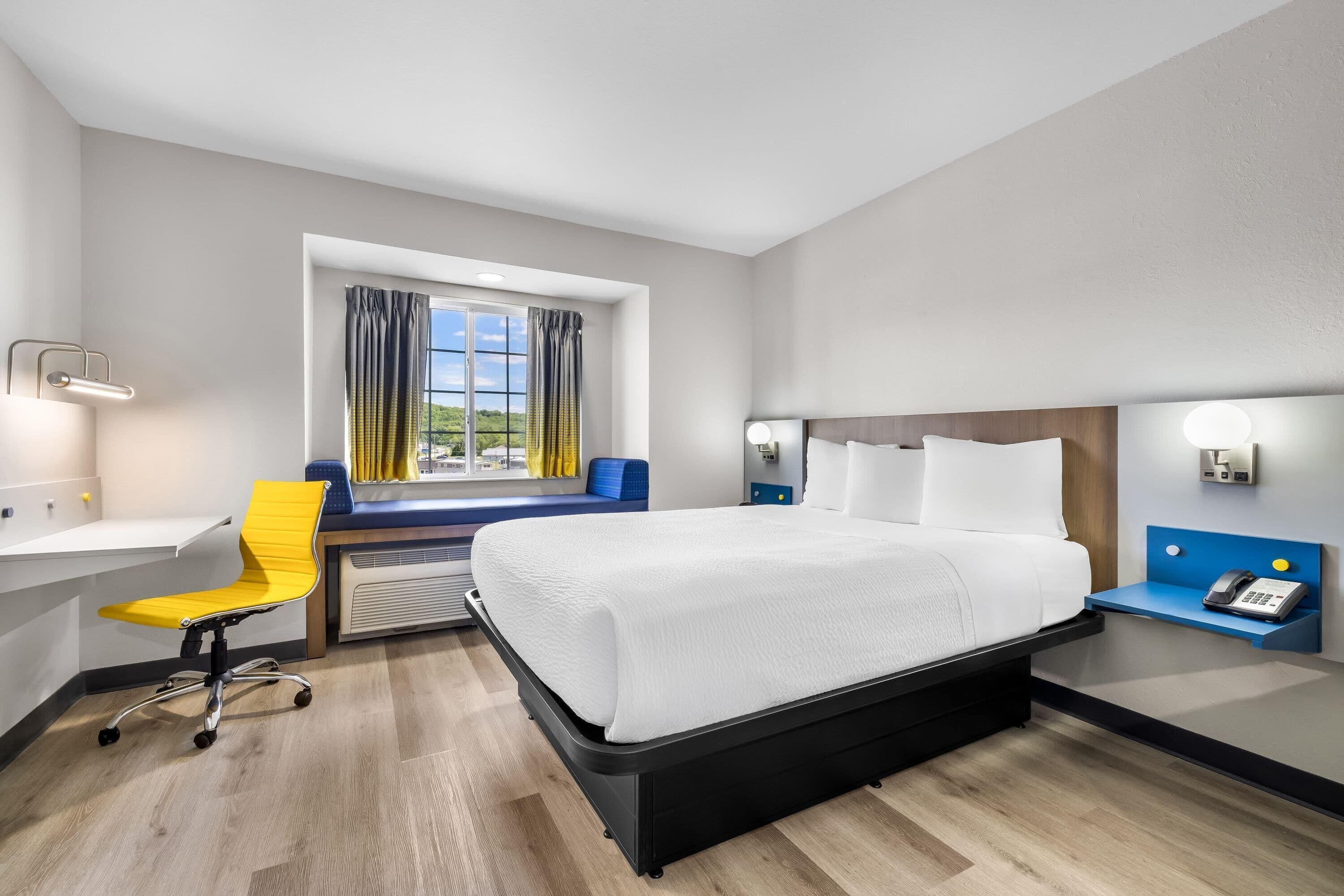 A hotel room with a bed, desk, chair, and a window with curtains.
