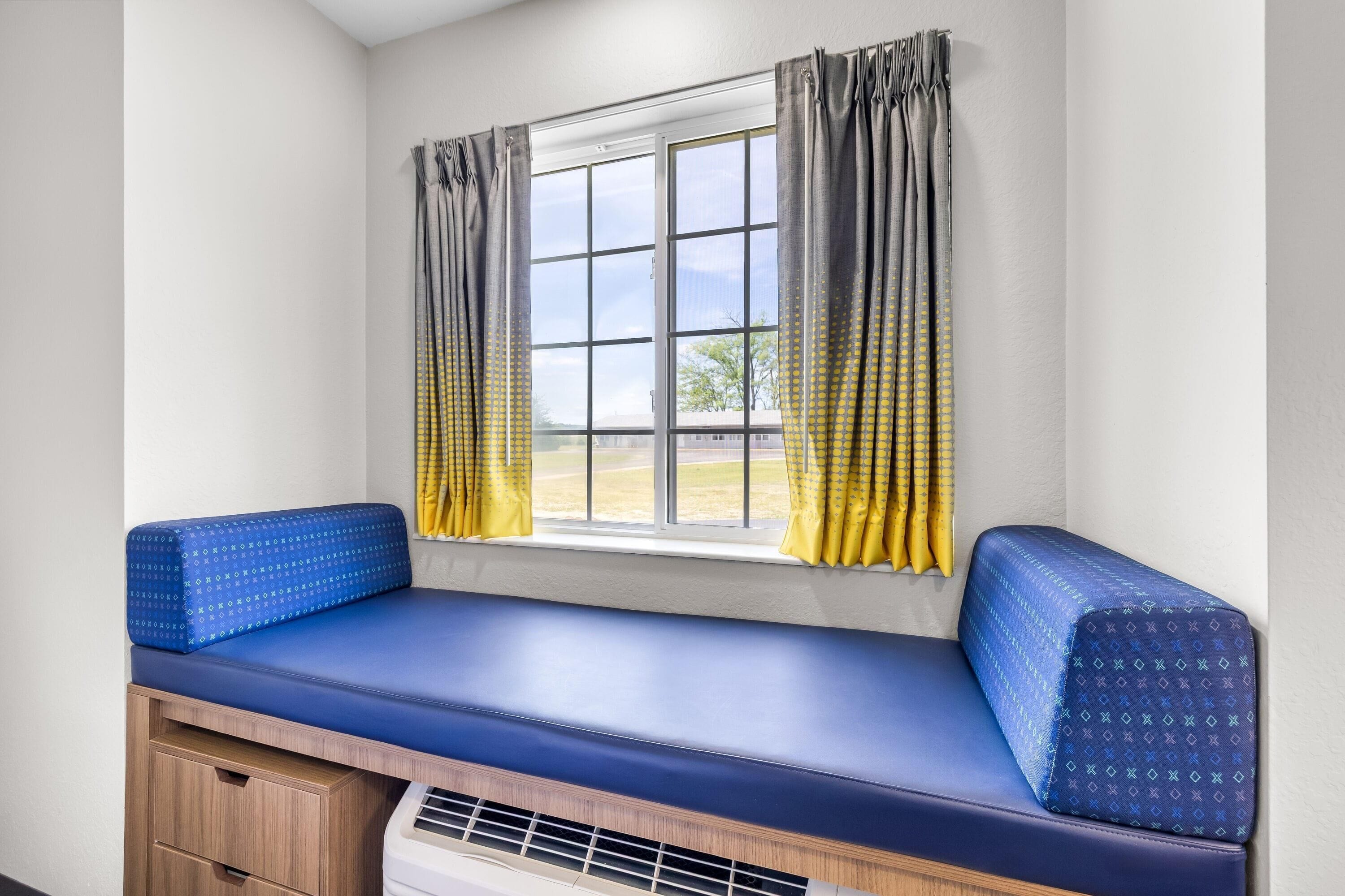 A window seat with a blue cushion, a small table, and a heater below.