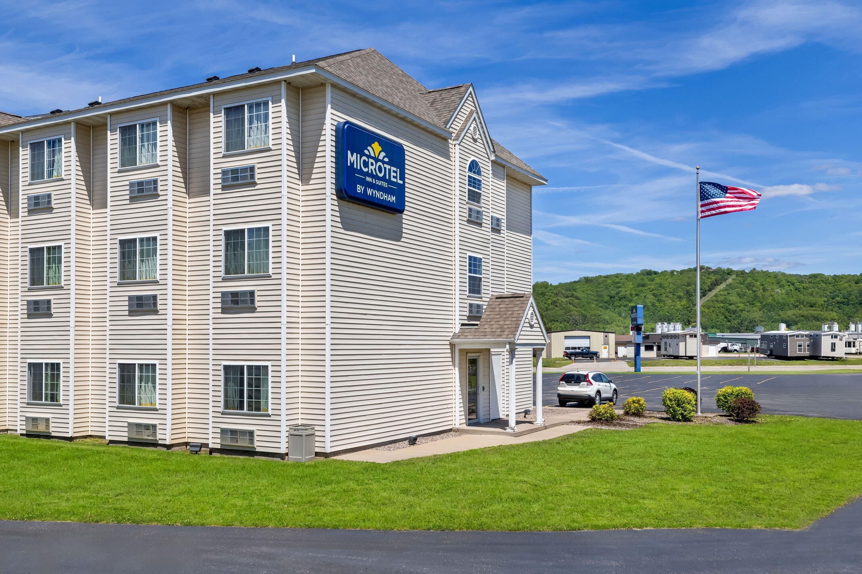 A Microtel Inn & Suites building with a flag, parking lot, and a grassy area.