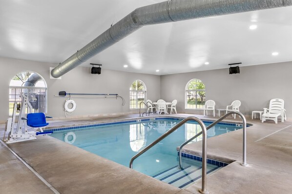 An indoor swimming pool with clear water, a diving board, and white chairs around the pool. - Microtel Inn & Suites by Wyndham Prairie du Chien (Prairie Du Chien)