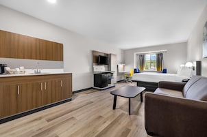 A modern hotel room with a kitchenette, a bed, a sofa, and a TV.