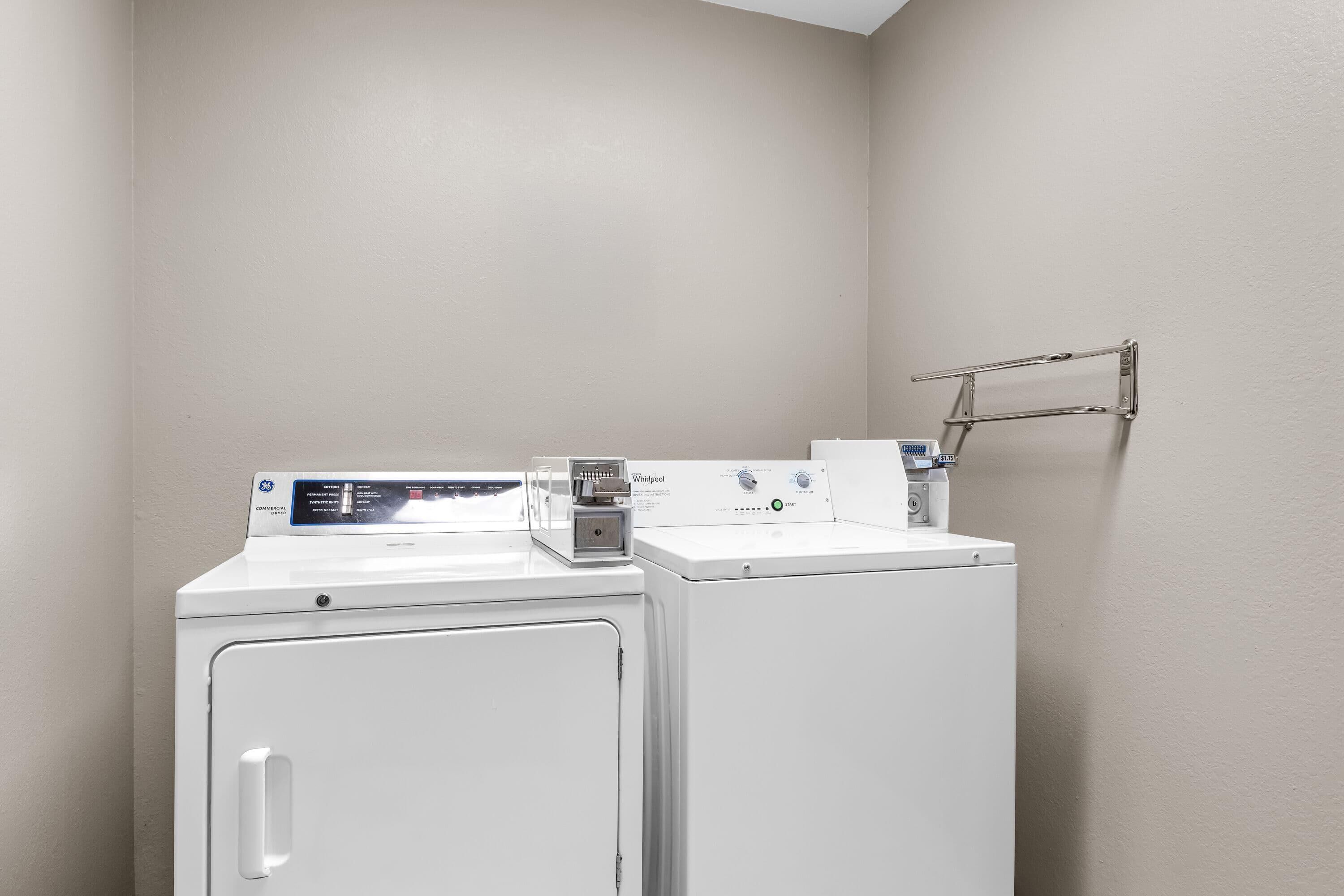 Une petite buanderie équipée de deux machines à laver et deux sèche-linge superposés, d’un étendoir métallique et d’un panneau de commande situé sur la machine à laver supérieure.