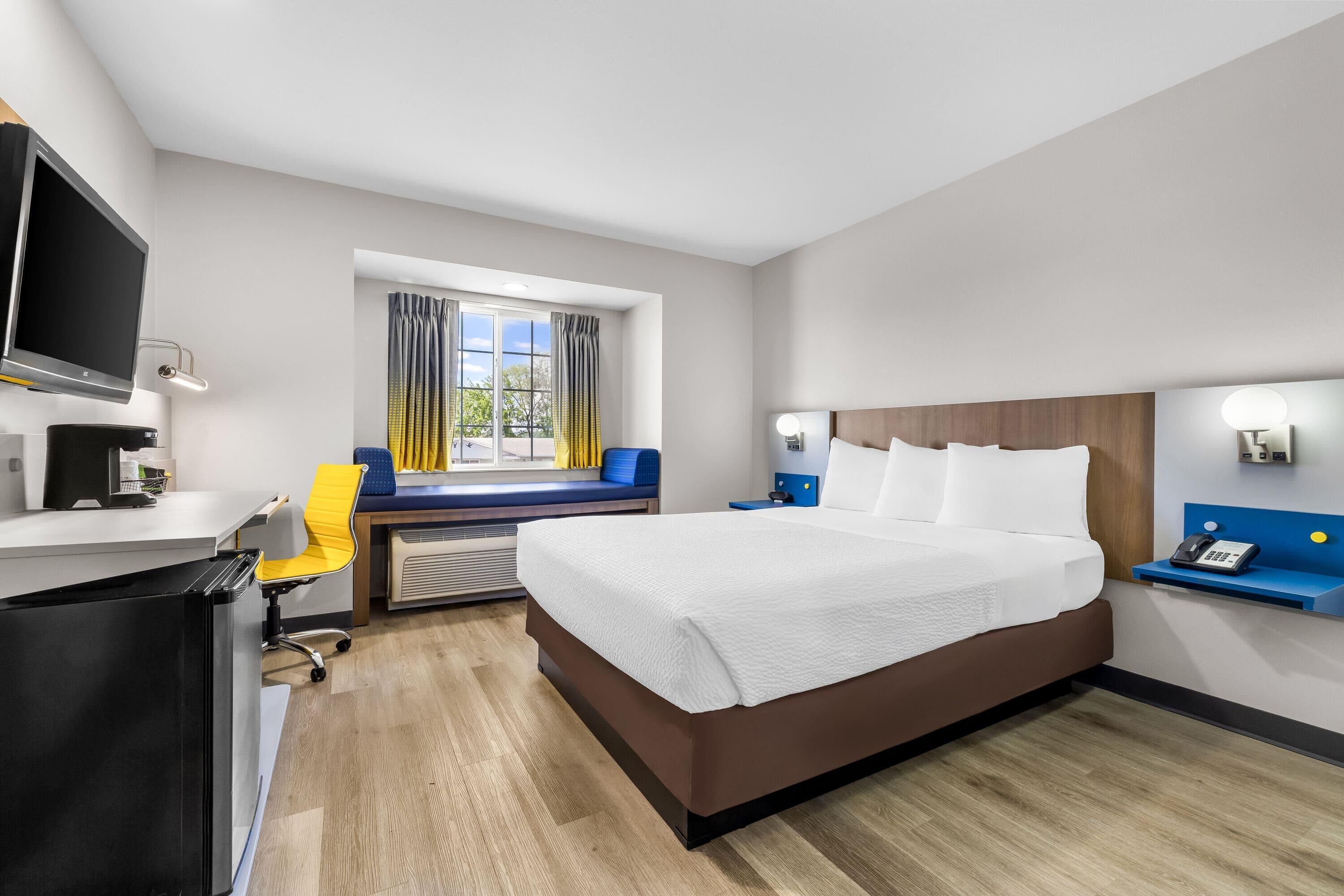 A hotel room with a bed, desk, chair, TV, and a window with curtains.