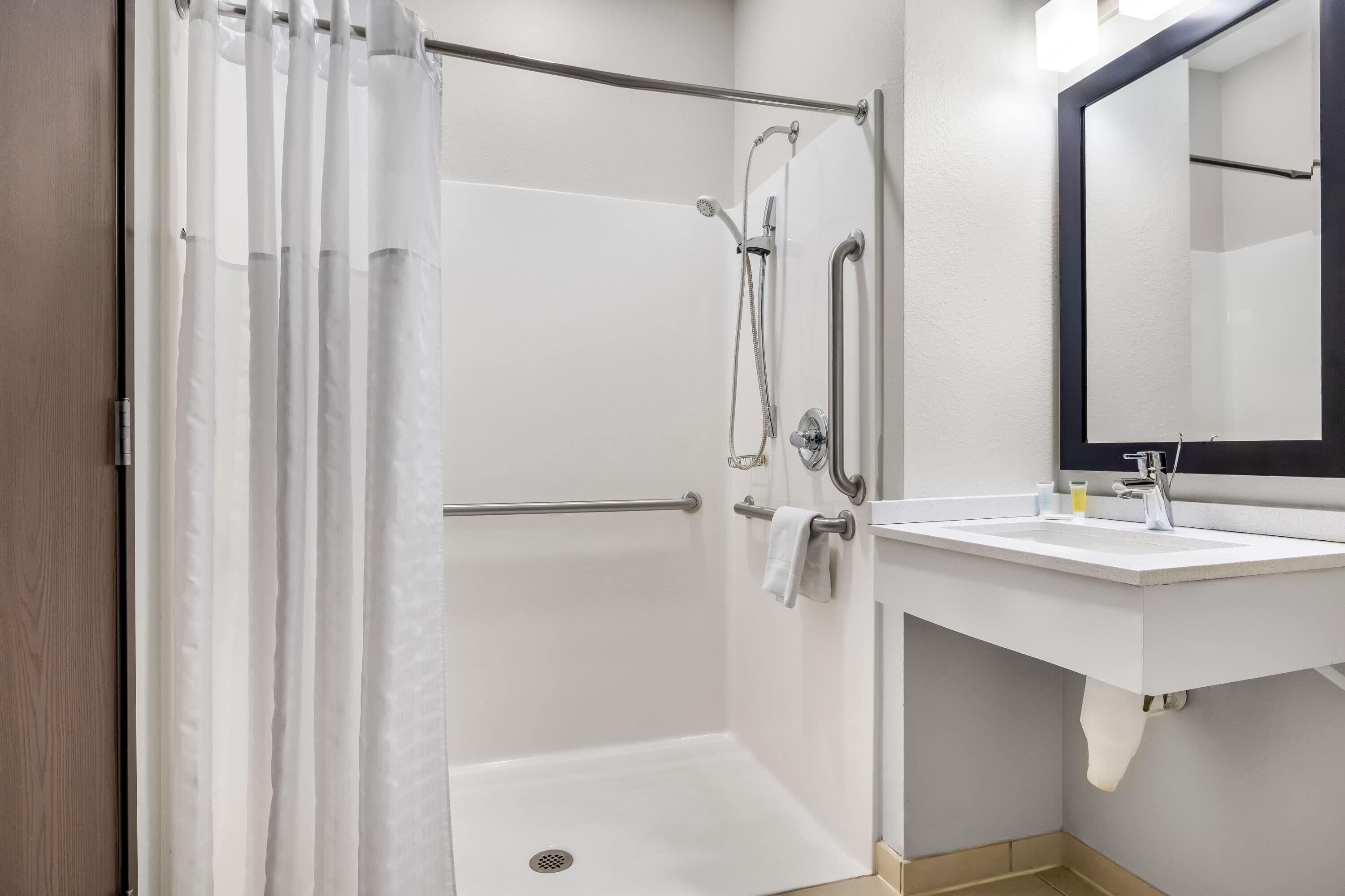 A shower with a glass door, a white sink with a mirror, and a towel rack.