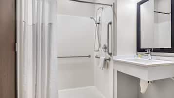 Una ducha con puerta de vidrio, un lavamanos blanco con espejo y un perchero para toallas.