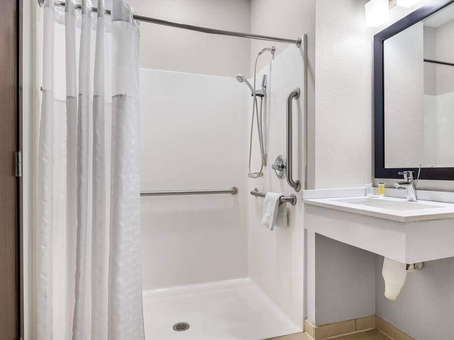 Una ducha con puerta de vidrio, un lavamanos blanco con espejo y un perchero para toallas.