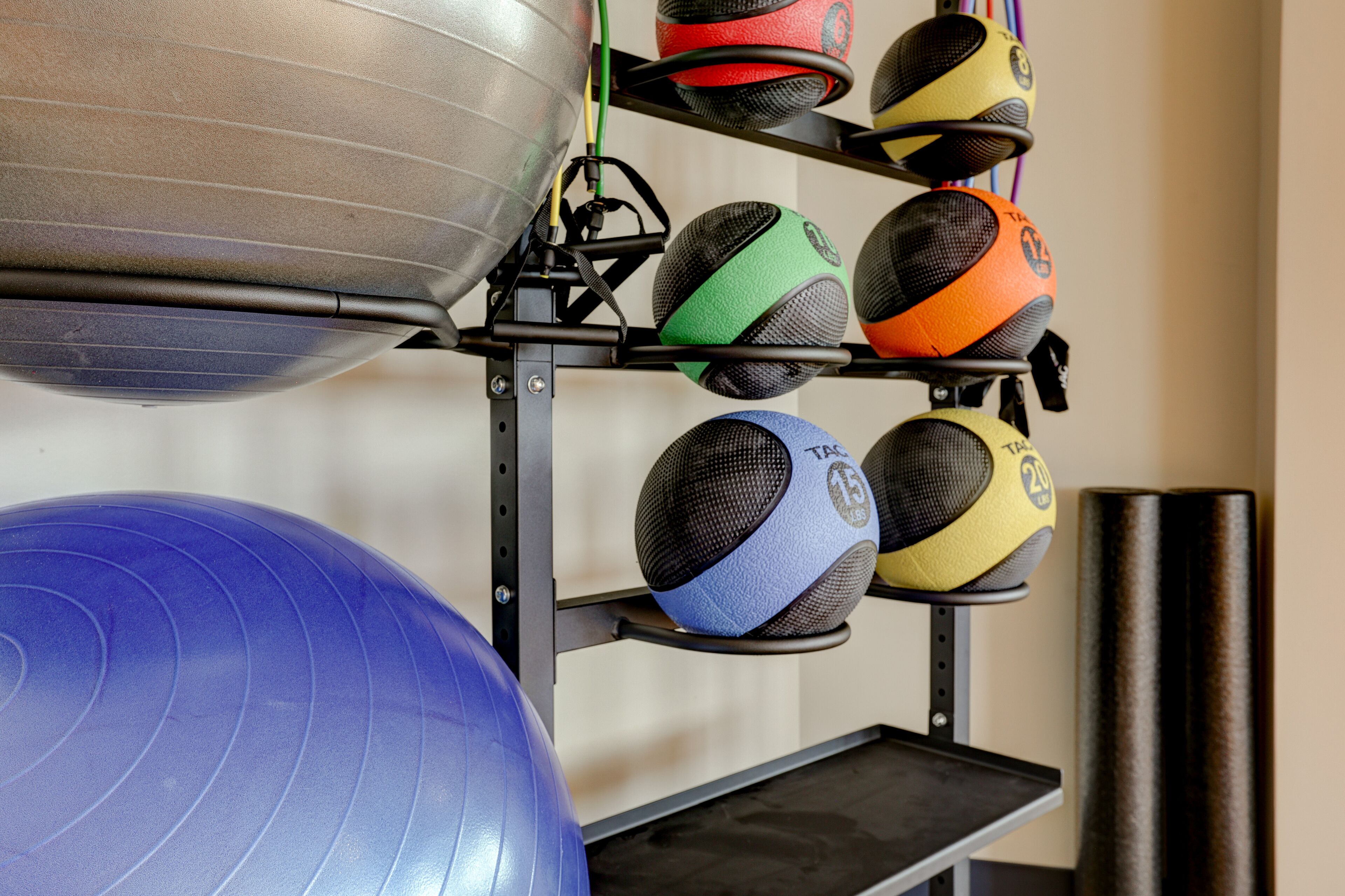 A gym with exercise equipment including a blue exercise ball, a metal kettle bell, and a rack with various medicine balls.