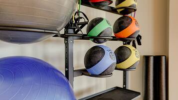 A gym with exercise equipment including a blue exercise ball, a metal kettle bell, and a rack with various medicine balls.