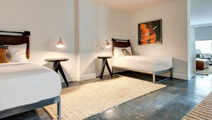 A modern hotel room with two beds, a small round table, a lamp, and a painting on the wall. - Elwood Hotel & Suites (Lexington)