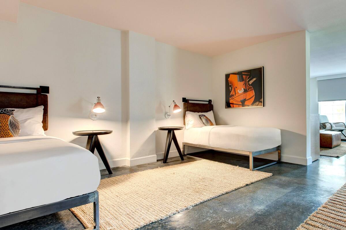 Ein modernes Hotelzimmer mit zwei Betten, einem kleinen runden Tisch, einer Lampe und einem Bild an der Wand.