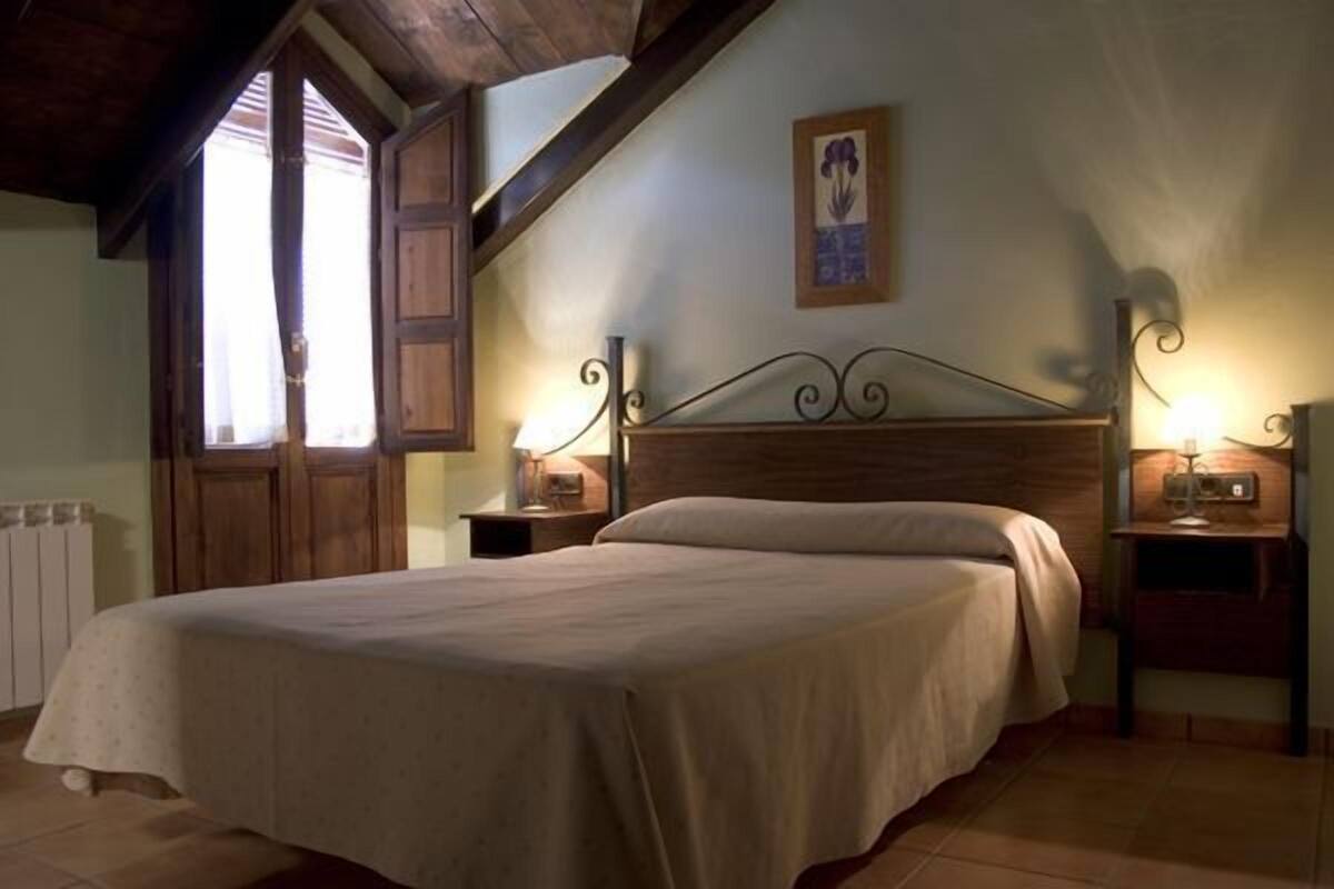 A bedroom with a wooden bed, two bedside tables with lamps, a window with shutters, and a framed picture on the wall.