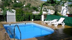 Una piscina con borde de baldosas, escalera metálica y sillas de descanso blancas.