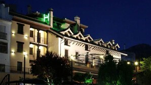 Un hotel con un estilo arquitectónico europeo tradicional, que cuenta con varios balcones y un llamativo letrero verde con la letra 'H', indicando el nombre del hotel.