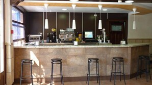 Zona de bar con mostrador, taburetes, máquina de café y televisor.
