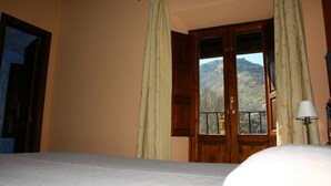Una habitación con cama, ventana con cortinas, puerta y vistas a montañas.