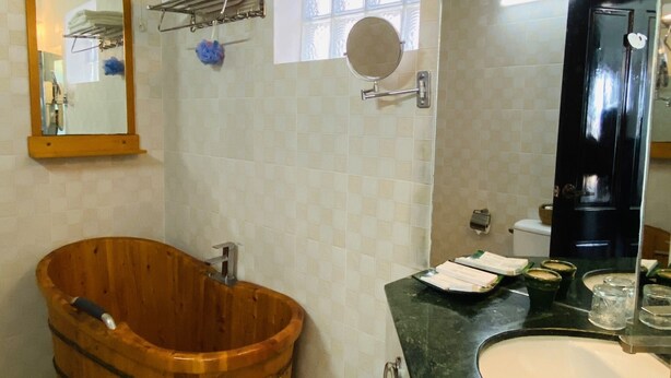 A bathroom with a wooden tub, a sink, a mirror, and a window.