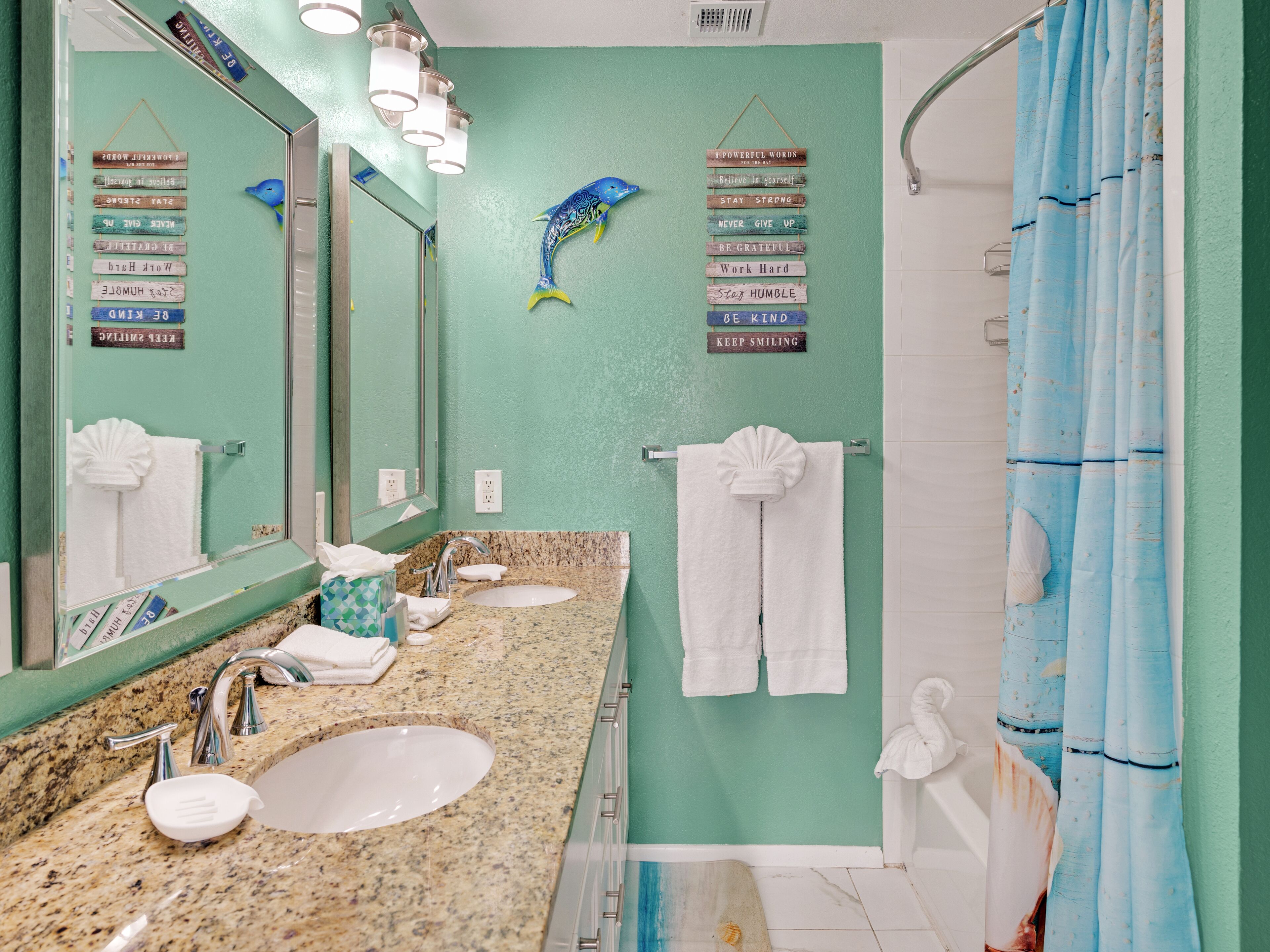 A bathroom with a green wall, two sinks, a large mirror, and a shower curtain.