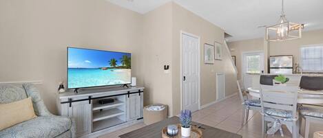 A living room with a flat-screen TV, a sofa, a coffee table, and a dining area with chairs and a table.