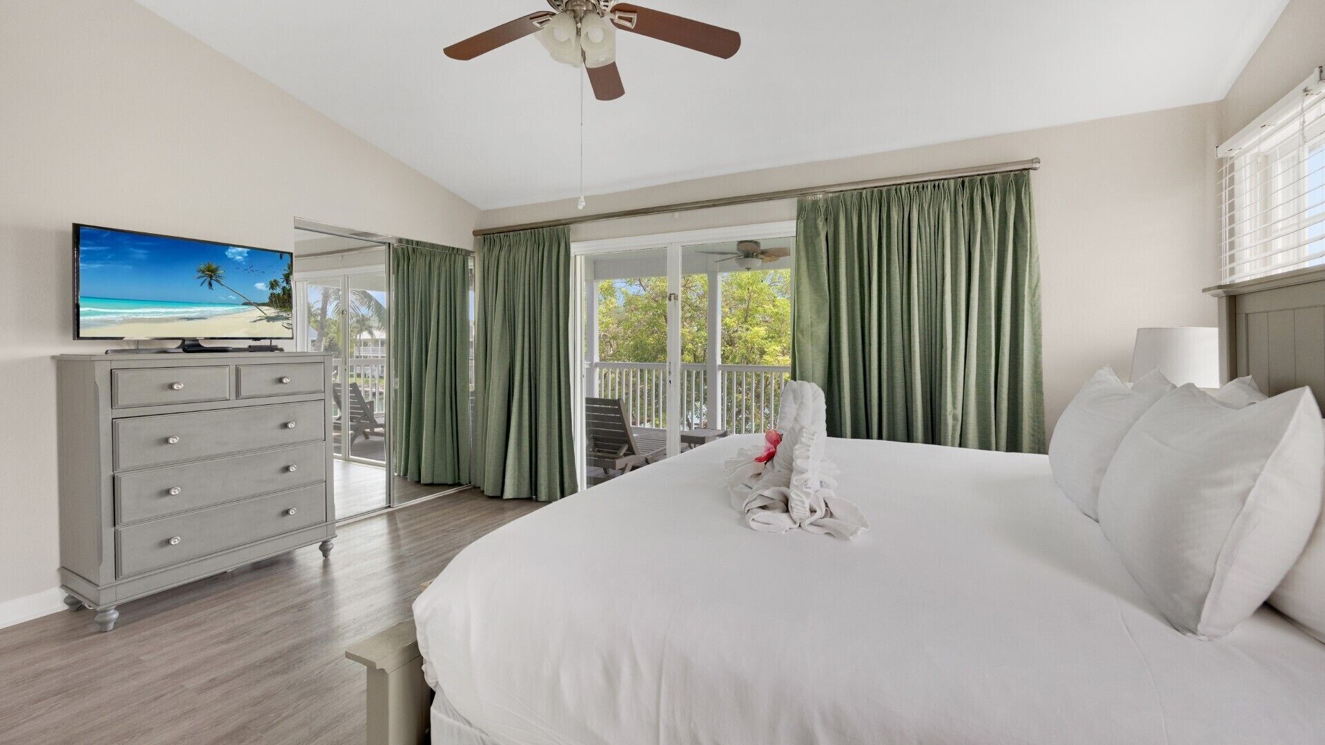 A hotel room with a bed, a dresser, a television, and a balcony with curtains.