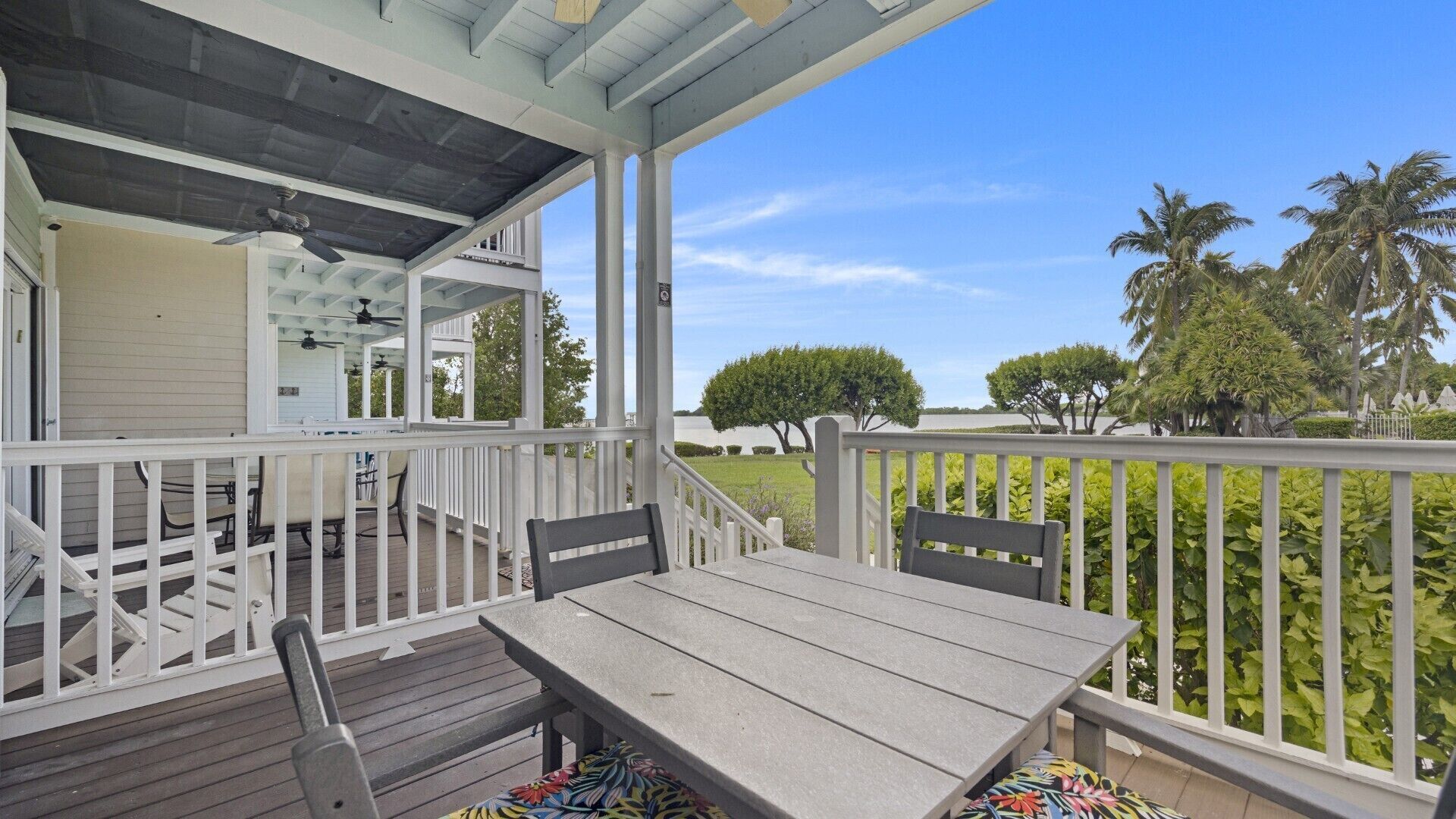 A covered outdoor area with a table and chairs, a ceiling fan, and a view of trees and a body of water.