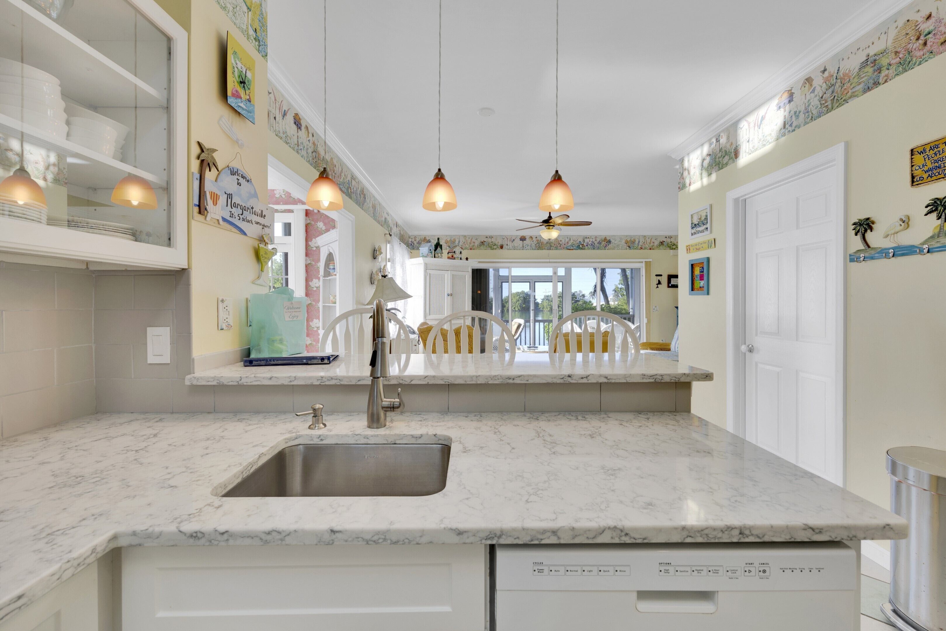A kitchen with a marble countertop, a built-in dishwasher, and pendant lights.