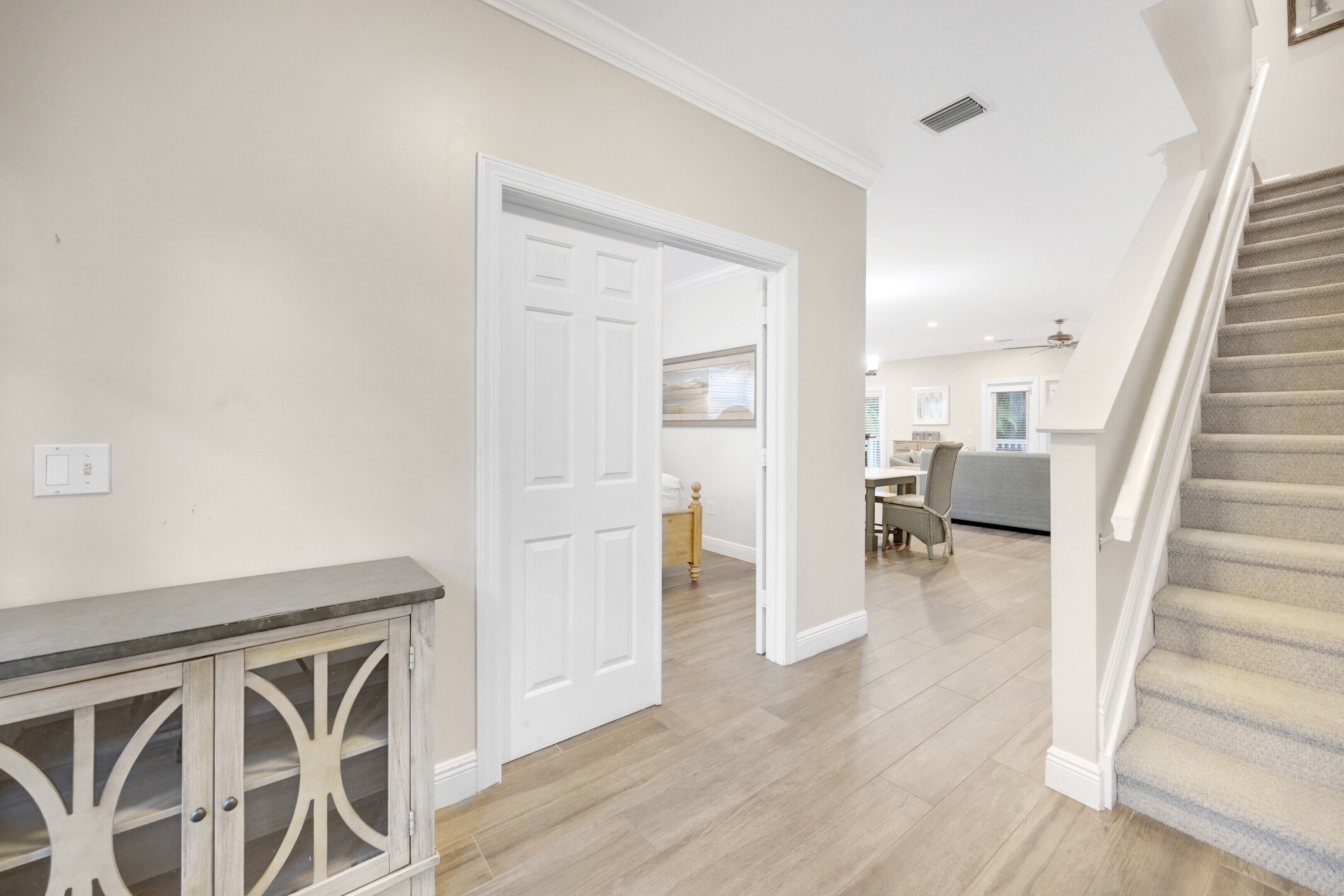 A hallway with a wooden floor, a white door, and a staircase with carpeted steps.