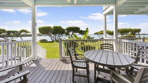 Eine überdachte Terrasse im Freien mit Tisch und Stühlen, mit Blick auf ein Gewässer und Bäume.