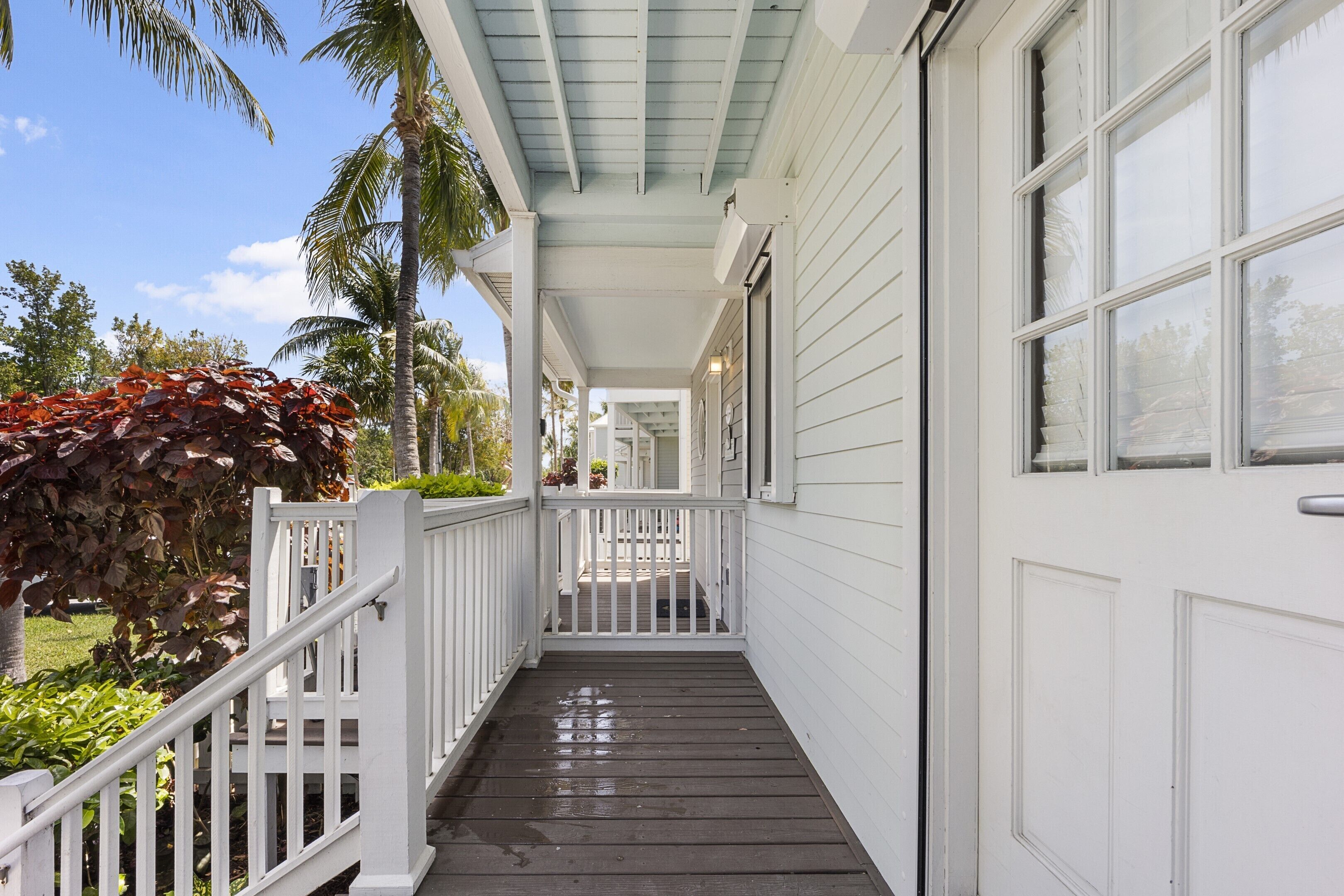 A covered wooden porch with white railings, leading to a white door.