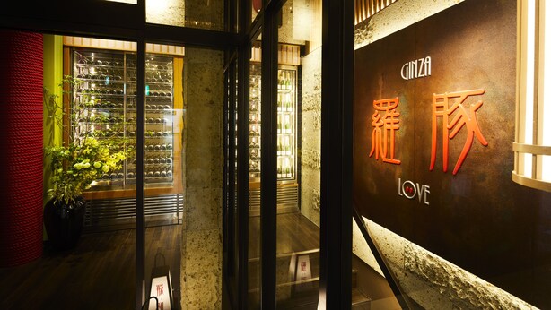 A hotel entrance with a glass door, a potted plant, and a wine rack visible through the glass. - Ginza Grand Hotel (Tokyo)