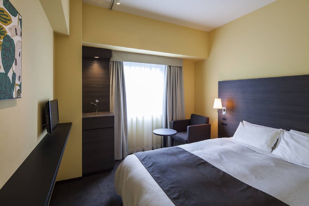 Hotellihuone, jossa on suuri sänky, työpöytä, tuoli, pieni pöytä ja televisio.