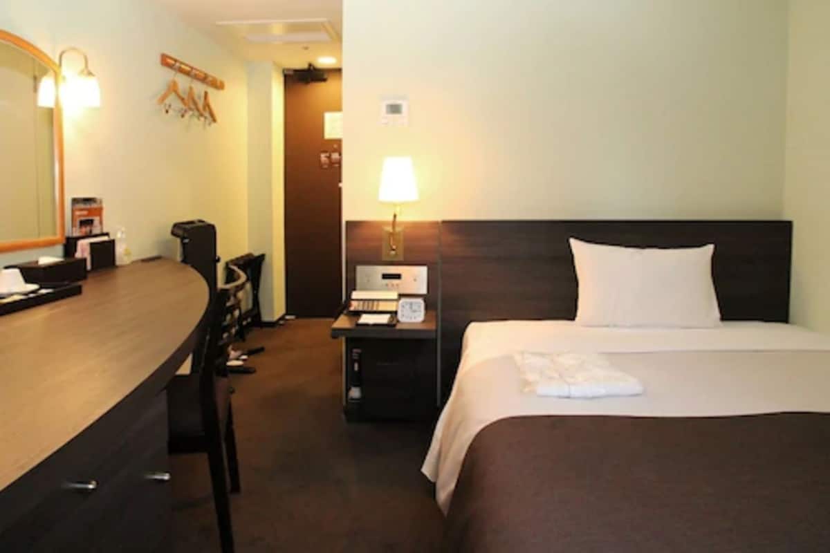 Hotellihuone, jossa on sänky, työpöytä, tuoli, lamppu ja peili.