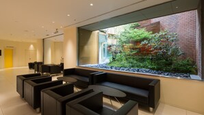 A modern lobby with black sofas, a coffee table, and a large window overlooking a garden. - Ginza Grand Hotel (Tokyo)