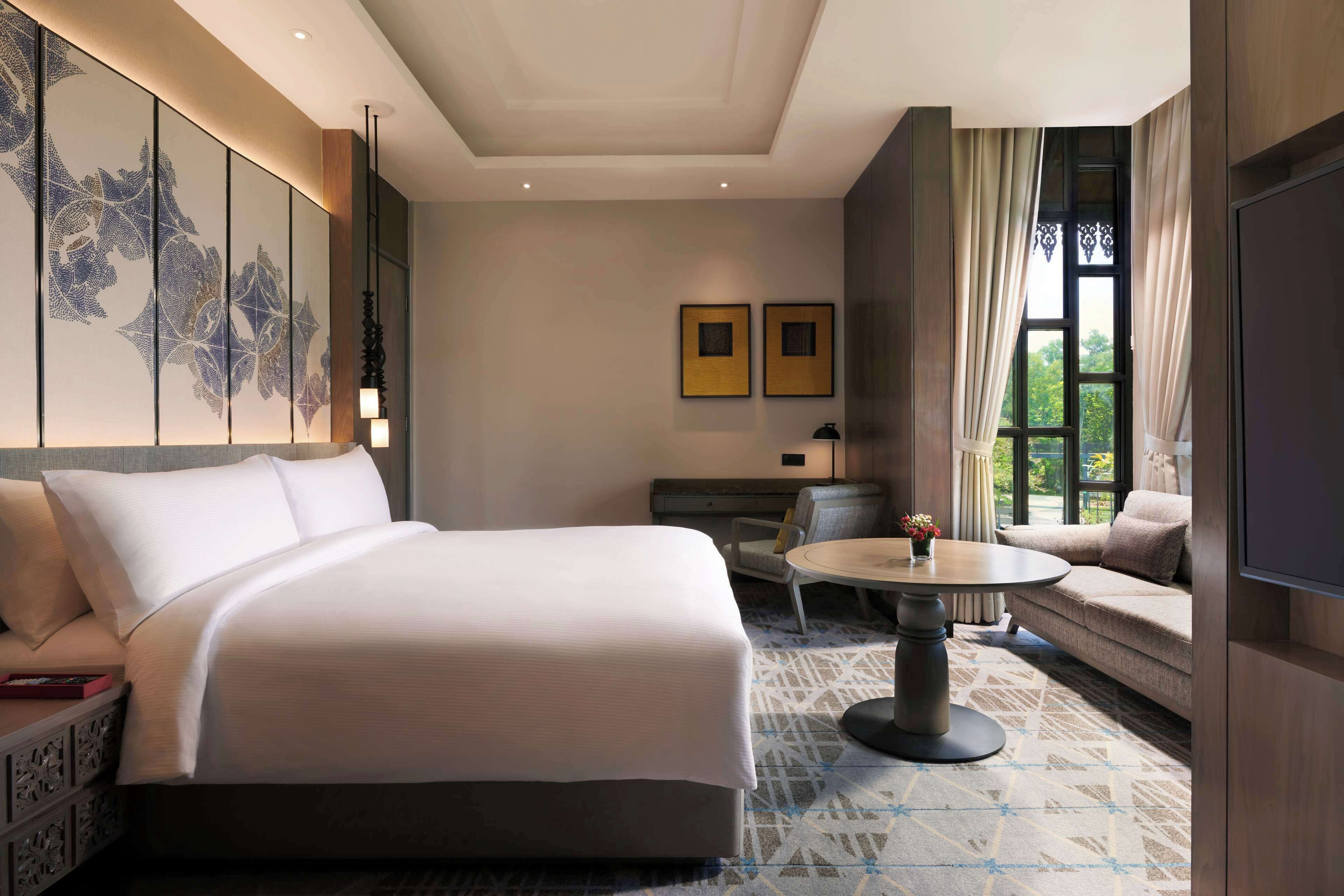 A hotel room with a large bed, a sofa, a dining table, and a TV.