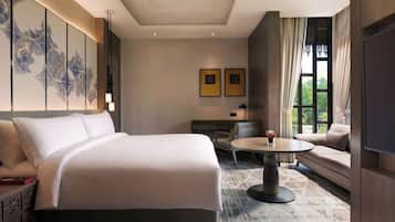 A hotel room with a large bed, a sofa, a dining table, and a TV.